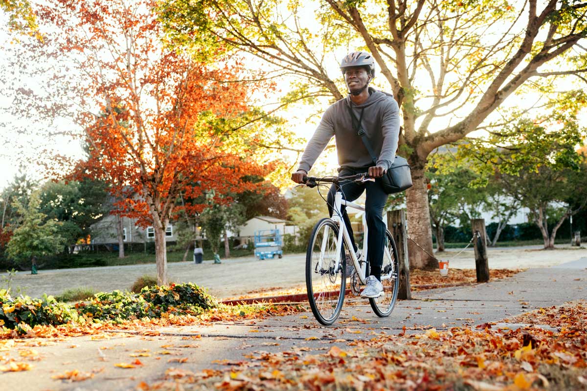 A man riding a bike with autumn leaves on the ground.