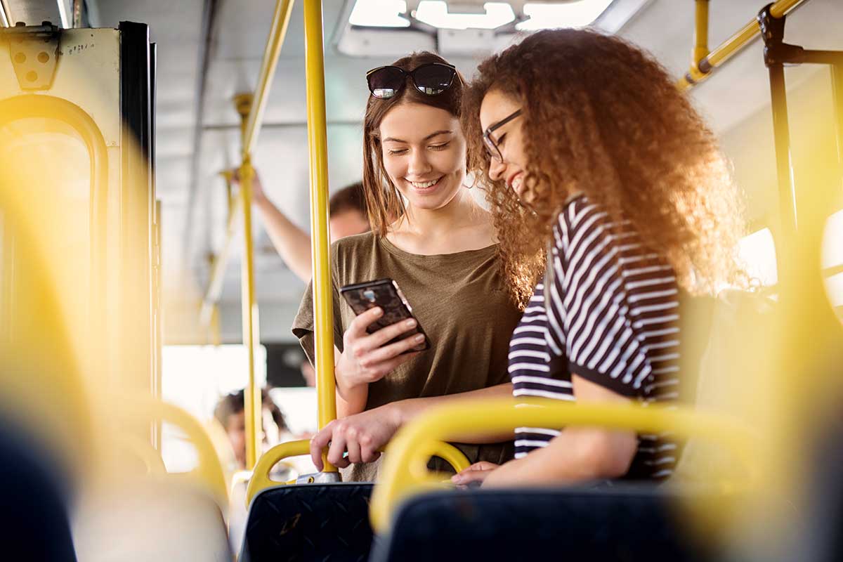 Two women on a bus using a mobile app to schedule their commute.